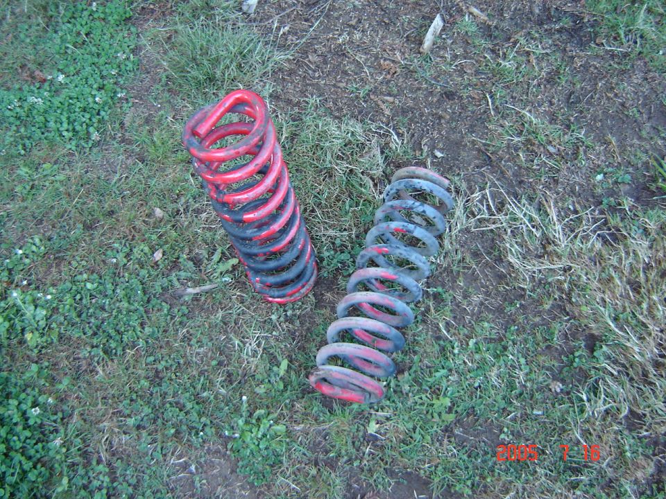 Two used coil springs, one red and black, one blue and red, lying on grass