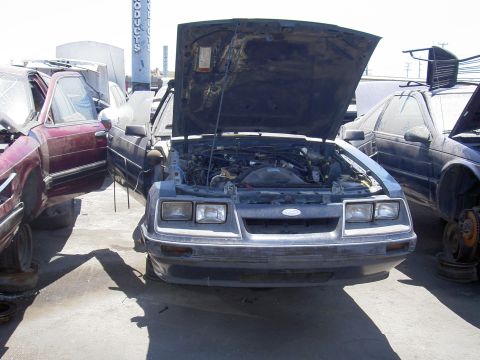 1982 Ford Mustang - This 1982 Ford Mustang is seen in a junkyard with its hood open, revealing the engine compartment.