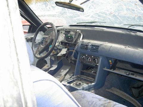 1982 Ford Mustang - The interior of a car shows significant damage and missing parts, including the dashboard and windshield.