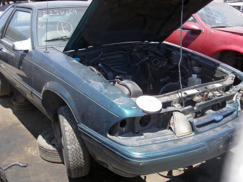 1982 Ford Mustang - Junkyard Mustang, hood up, showing engine bay and front damage. Another car is visible to the right.