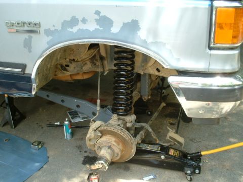 1991 Ford Bronco - Front suspension of a 1991 Ford Bronco undergoing repair, with a jack and tools visible.