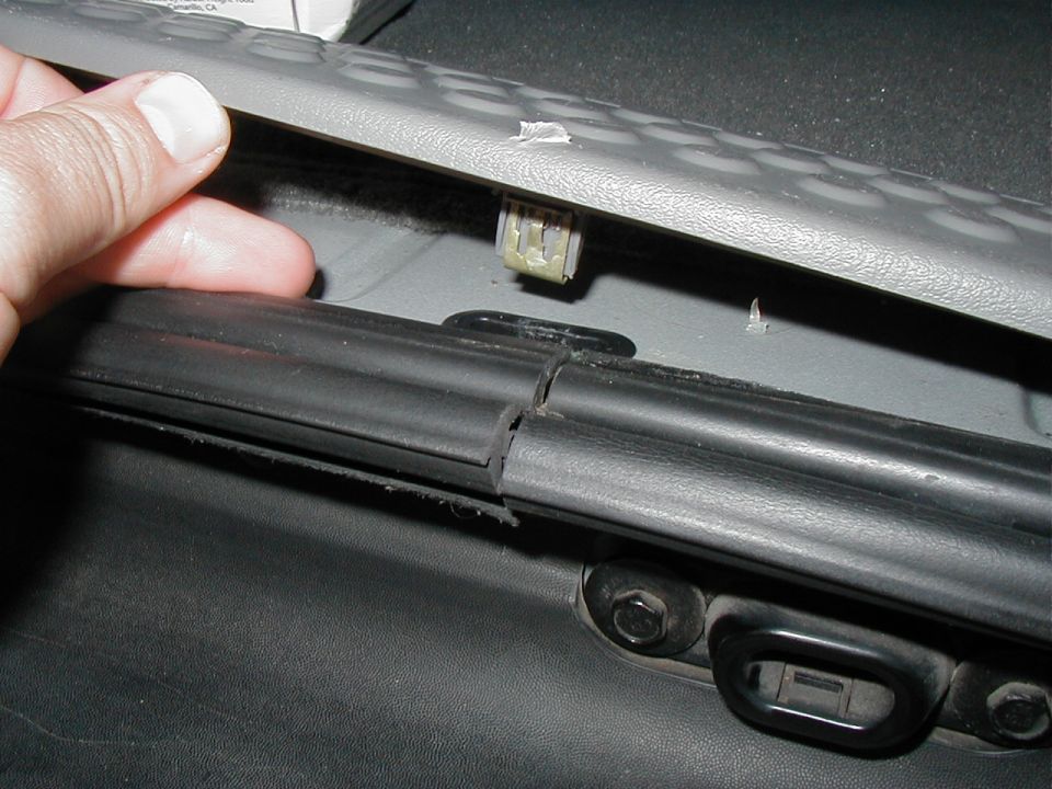Hand prying gray trim panel exposing white clip and black weatherstrip in vehicle interior