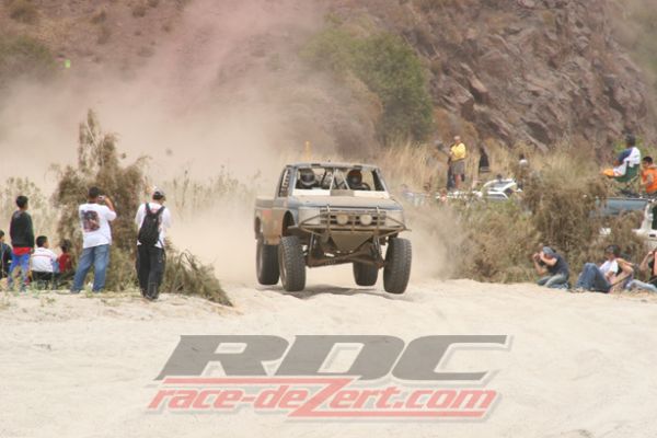 Off-road race truck jumping over a berm as spectators watch