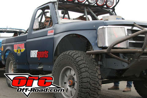 1990 Ford Bronco - dark blue tube-chassis off-road race truck with Dirt Sports decals sits staged, with an Off-Road.com watermark.