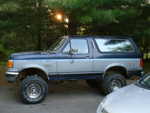 1991 Ford Bronco - A lifted 1991 Ford Bronco is parked outdoors, showing its two-tone paint and side profile.
