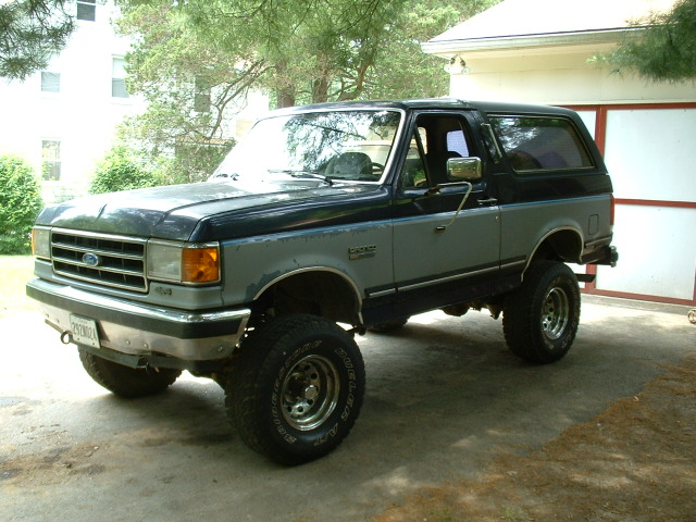 Two-tone Ford Bronco parked in front of a garage. It has large off-road tires and a lifted suspension