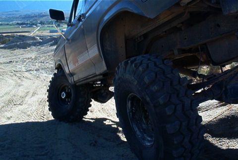 1986 Ford Bronco - This SUV is equipped with large off-road tires and is driving on a sandy, hilly terrain.
