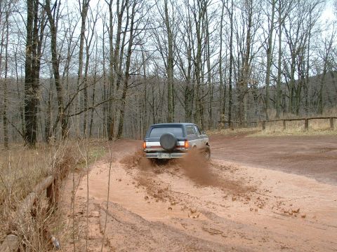 1991 Ford Bronco - A 1991 Ford Bronco navigates a muddy trail, sending dirt flying.