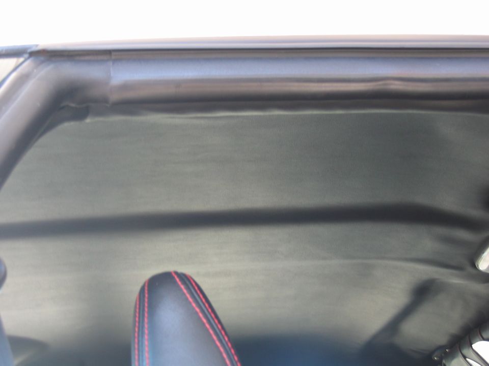 Black vehicle headliner and pillar with a red-stitched leather seat below