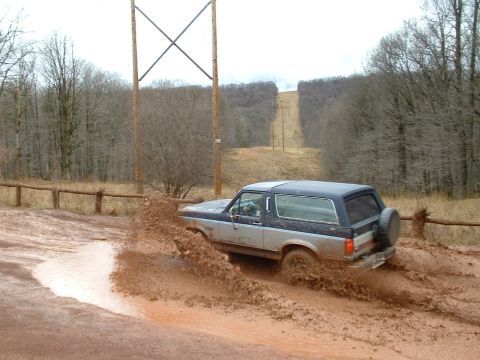 1991 Ford Bronco - A 1991 Ford Bronco navigates a muddy off-road path, sending dirt flying.