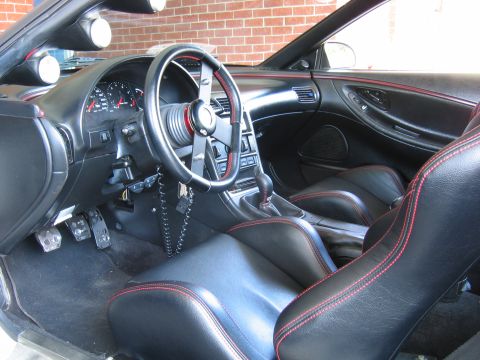 1993 Ford Probe - Interior view of a car with black seats and red stitching, custom steering wheel, and dashboard gauges.