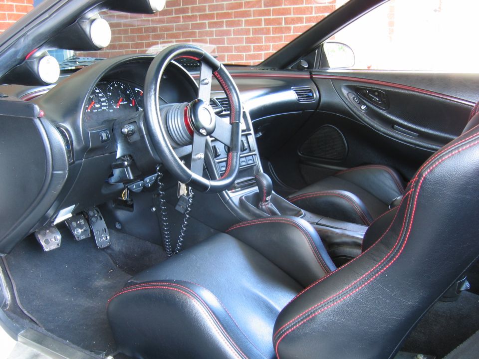 Car interior showing dashboard, steering wheel, seats with red stitching, and gear shifter