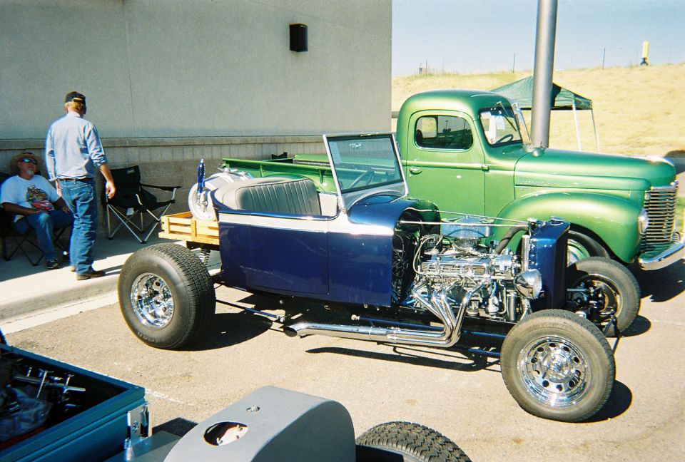 Blue custom roadster with exposed engine next to a green vintage pickup truck