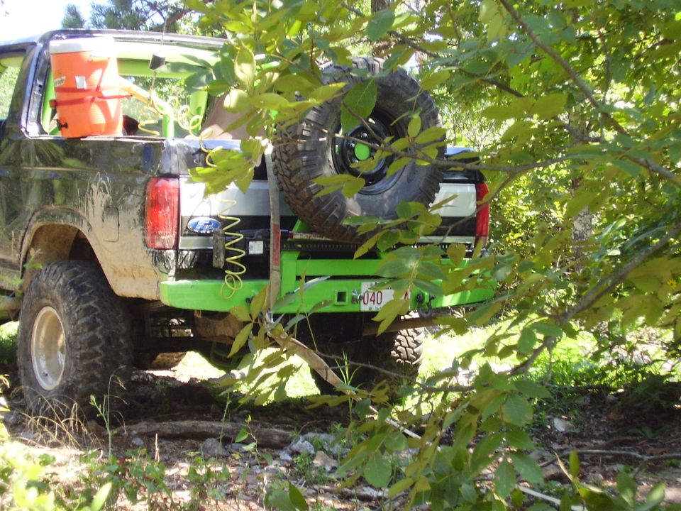 Green Ford Bronco with tube bumper and spare tire carrier among brush