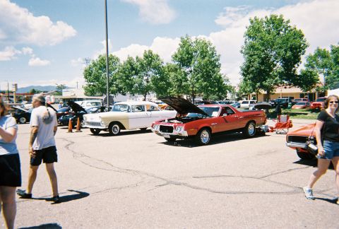 1972 Ford Ranchero - A red pickup truck is displayed at an outdoor car show with its hood open, alongside other vehicles.