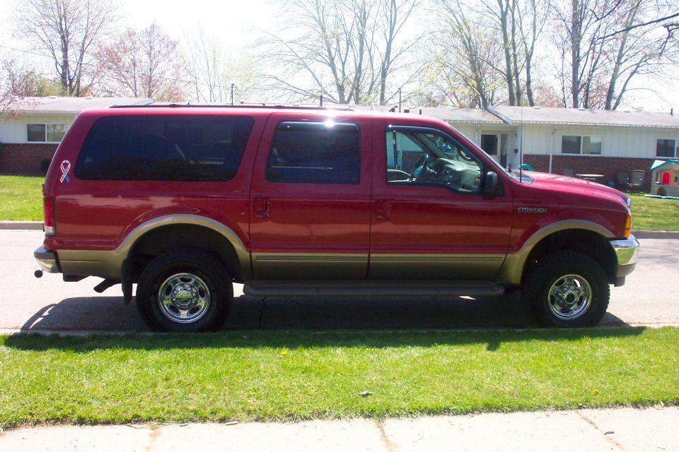 Red Ford Excursion SUV with tan lower cladding, side view, parked at a suburban curb