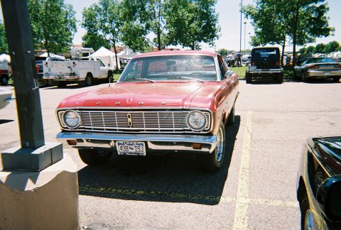 1972 Ford Ranchero - A red Ford sedan is parked in a lot, with other vehicles and trees in the background.