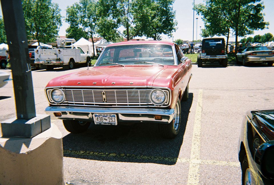 Red Ford Falcon front view parked at a sunny car show lot