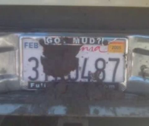 1988 Ford Bronco - The license plate is heavily caked in mud, obscuring most of the details except for the phrase 'GO MUD?!' and the numbers '3J487'.