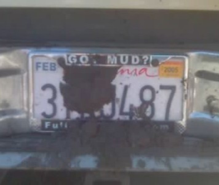 Mud-covered California license plate in "Go Mud?" frame on a chrome bumper
