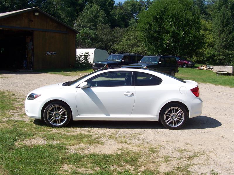 White Scion tC coupe parked on gravel near a barn and other vehicles