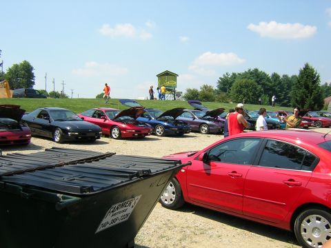 1995 Ford Probe - A collection of cars are gathered outdoors on a sunny day, with several having their hoods open.