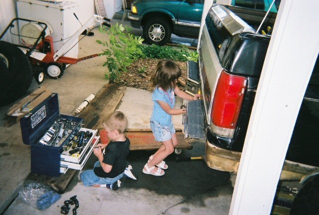 Two children playing with tools beside a pickup tailgate in a garage