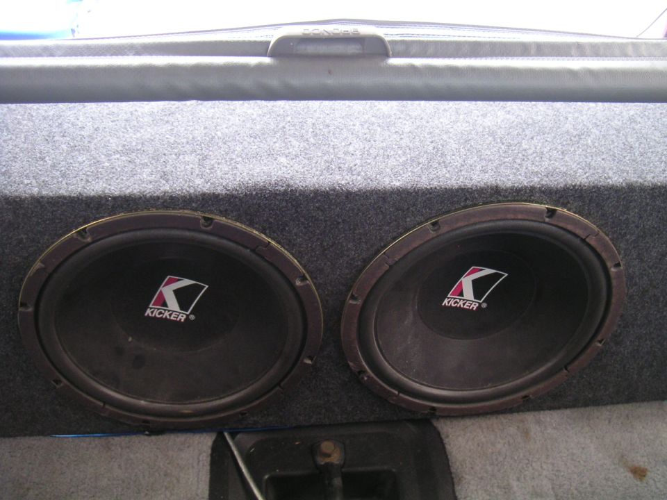 two Kicker subwoofers in a gray carpeted box