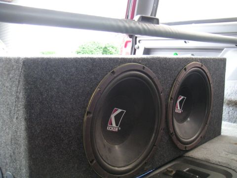 1994 Ford Bronco - A close-up view of dual Kicker subwoofers mounted in a gray carpeted enclosure within a vehicle's cargo area.
