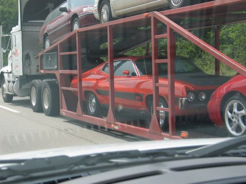1995 Ford Bronco - A red muscle car is being transported on a car carrier truck alongside other vehicles.