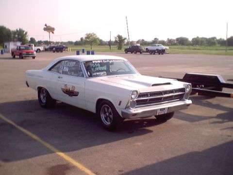 1967 Ford Fairlane - White 1967 Ford Fairlane drag car with racing decals and hood scoop sits on asphalt.