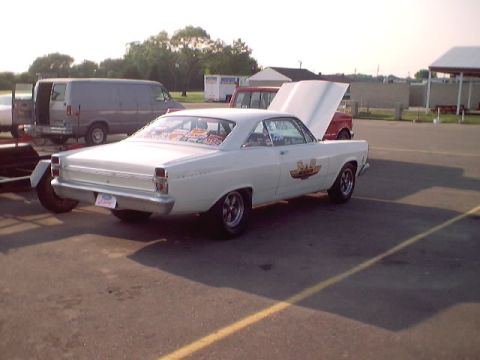 1967 Ford Fairlane - A white 1967 Ford Fairlane coupe is parked with its hood open, displaying racing decals on the door and stickers on the rear window.