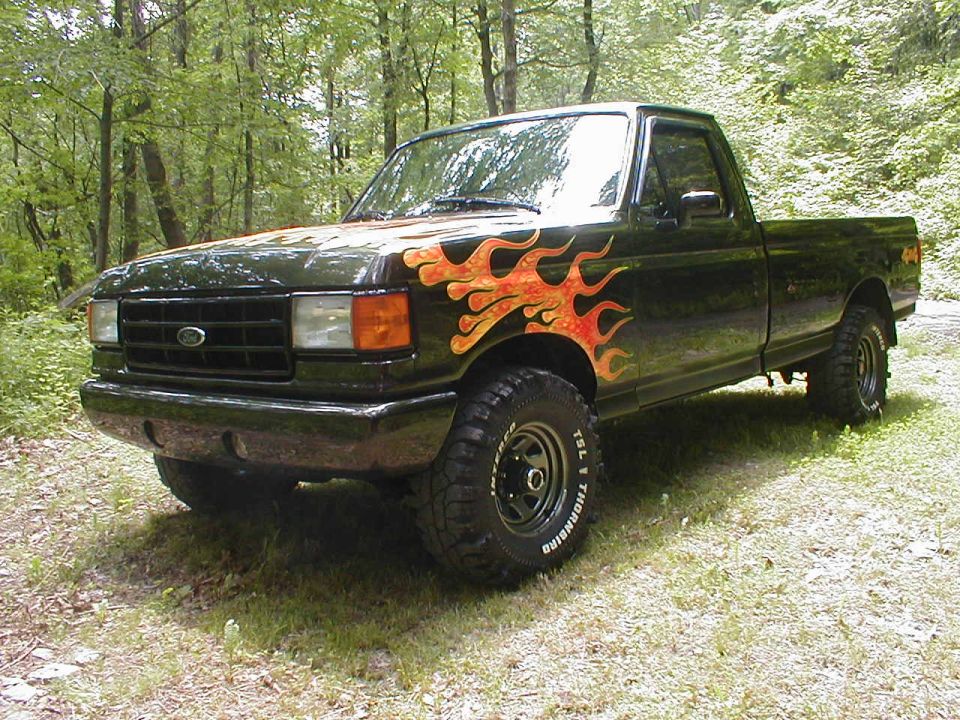 Black 1991 Ford F-150 pickup truck with flame decals on the hood and front fenders, lifted suspension, and off-road tires