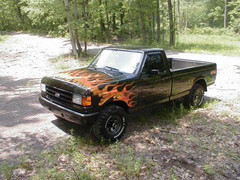 1991 Ford F-150 - This 1991 Ford F-150 features custom flame decals on the hood and front fenders, parked in a wooded area.