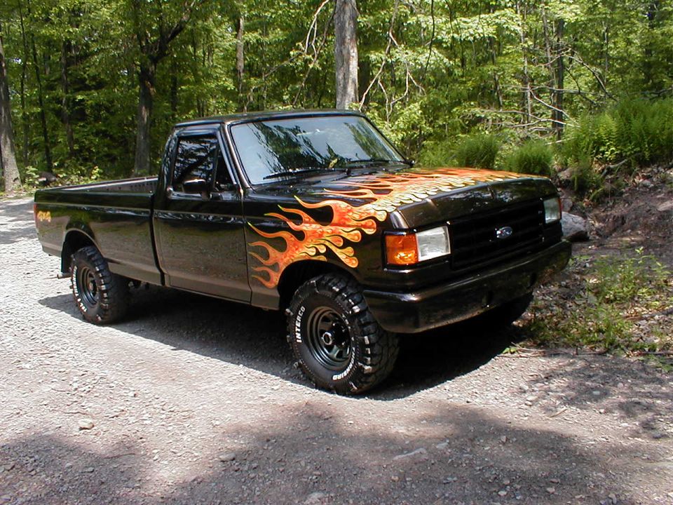 1991 Ford F-150 pickup truck with flame decals on hood and fender, parked on a dirt road