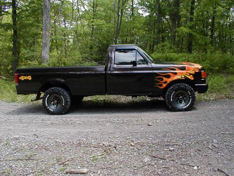 1991 Ford F-150 - This black Ford F-150 pickup truck features flame graphics on the front fender and hood, with "4x4" badging on the rear quarter panel.