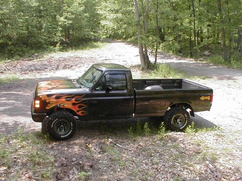 1991 Ford F-150 - A black pickup truck with flame decals is parked on a dirt road in a wooded area.