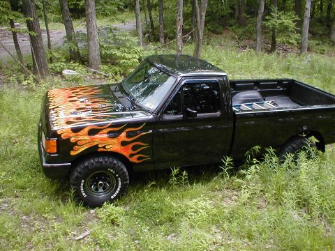 1991 Ford F-150 - This 1991 Ford F-150 features custom flame decals on the hood and fender, parked amidst trees.
