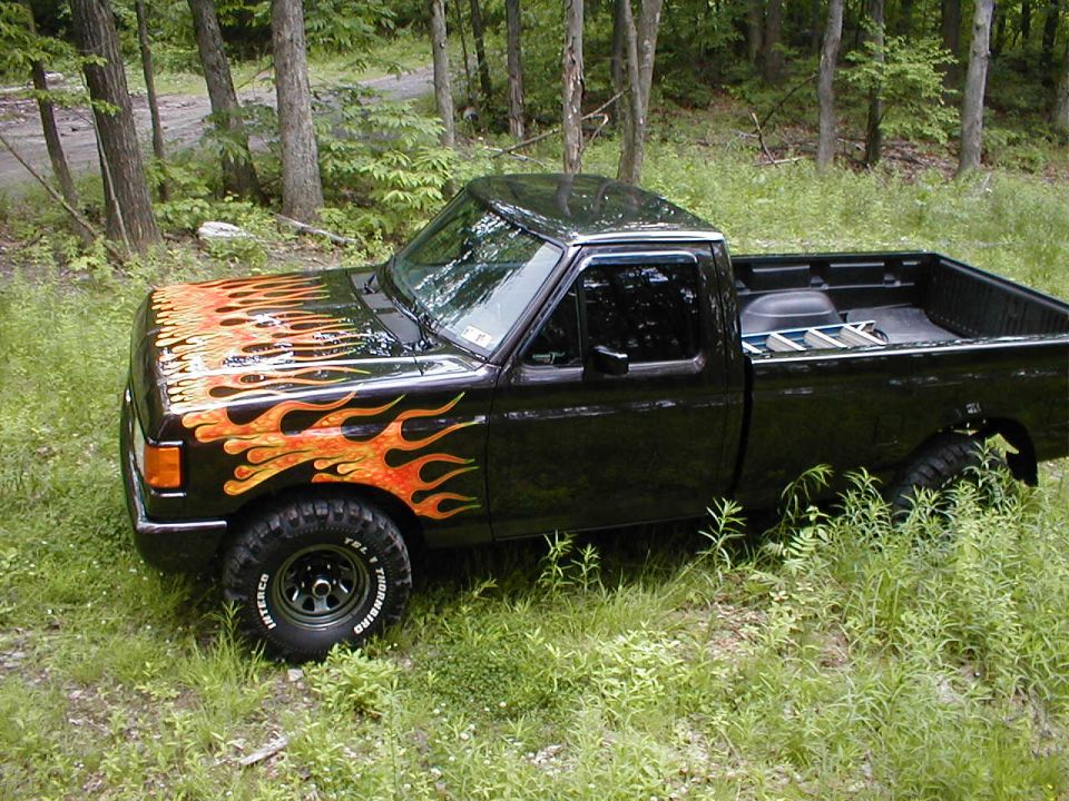 Black 1991 Ford F-150 with flame decals parked in a wooded area