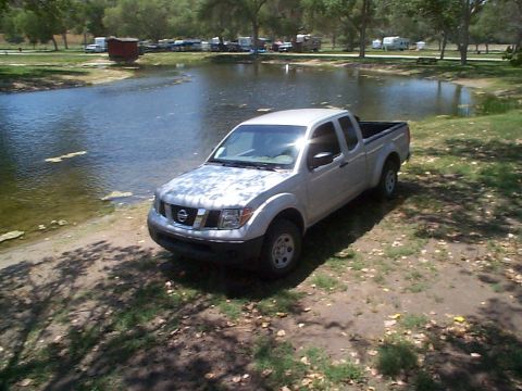 2005 Nissan Frontier - A silver Nissan Frontier pickup truck is parked on the grassy shore of a lake on a sunny day.
