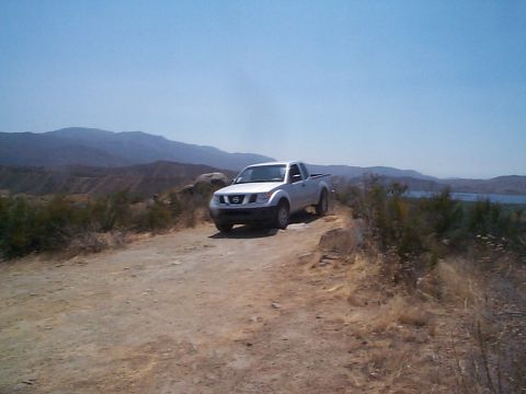 2005 Nissan Frontier - A white Nissan Frontier pickup truck is parked on a dirt road in a dry, hilly landscape.