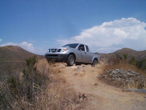 2005 Nissan Frontier - A silver 2005 Nissan Frontier navigates a , off-road trail under a partly cloudy sky.