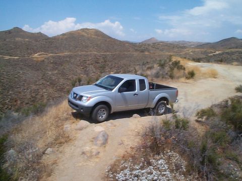 2005 Nissan Frontier - A silver 2005 Nissan Frontier pickup truck navigates a dusty, arid landscape under a clear blue sky.