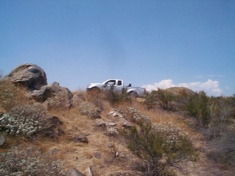 2005 Nissan Frontier - A white pickup truck navigates a , arid landscape with sparse vegetation and large rocks.