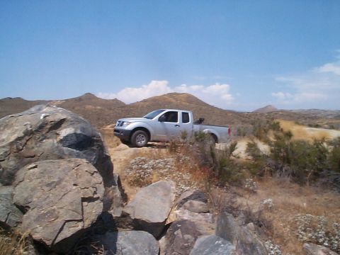 2005 Nissan Frontier - A silver 2005 Nissan Frontier pickup truck navigates a , dry terrain under a clear blue sky.