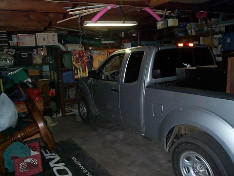 2005 Nissan Frontier - A silver 2005 Nissan Frontier pickup truck is parked inside a garage filled with various items.