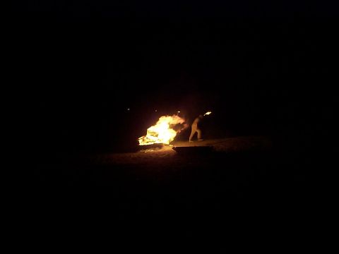2005 Nissan Frontier - A person stands near a fire at night, holding a torch.