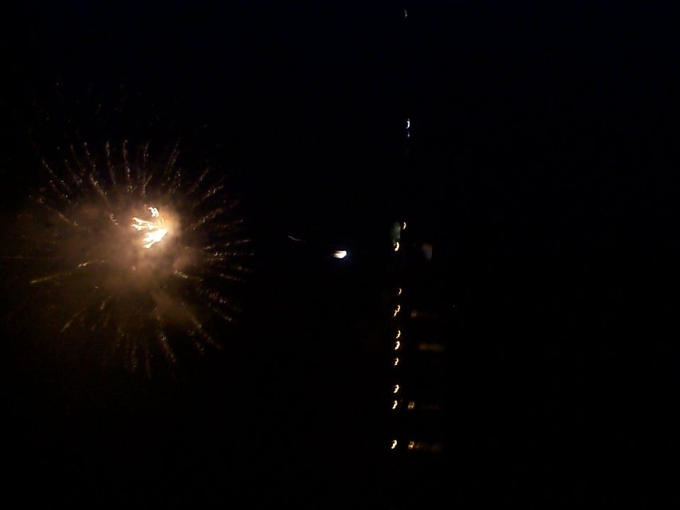 Fireworks explode in a dark sky near a tall tower with illuminated windows