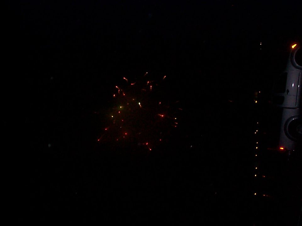 Part of a dark vehicle with lights and fireworks in the background