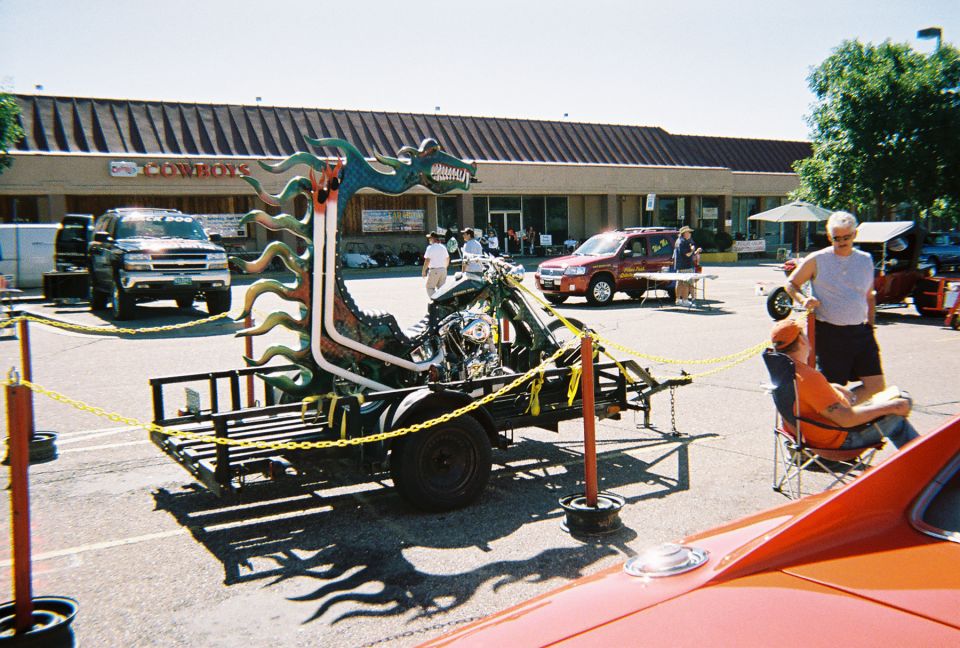 Green dragon-themed custom chopper on a flatbed trailer at an outdoor car show